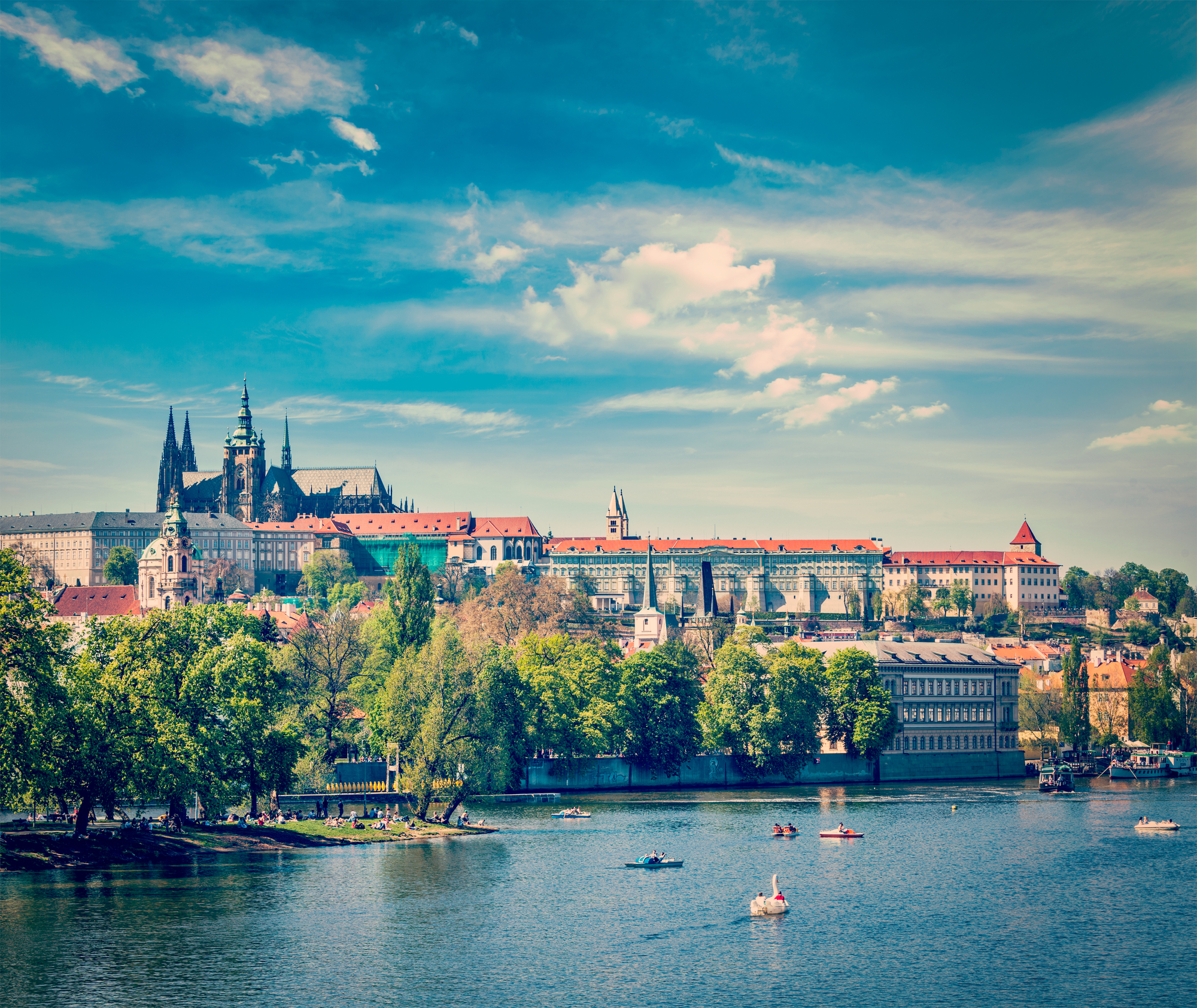 Vintage retro hipster style travel image of panorama view of Vltava river and Gradchany (Prague Castle) and St. Vitus Cathedral and Charles bridge an people in paddle boats in the Prague, Czech Republic